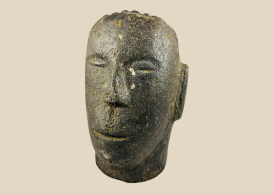 Antique Polynesian volcanic stone head sculpture, carved with stylized facial features and linear hair details, used for ancestor veneration, photographed on a white background.
