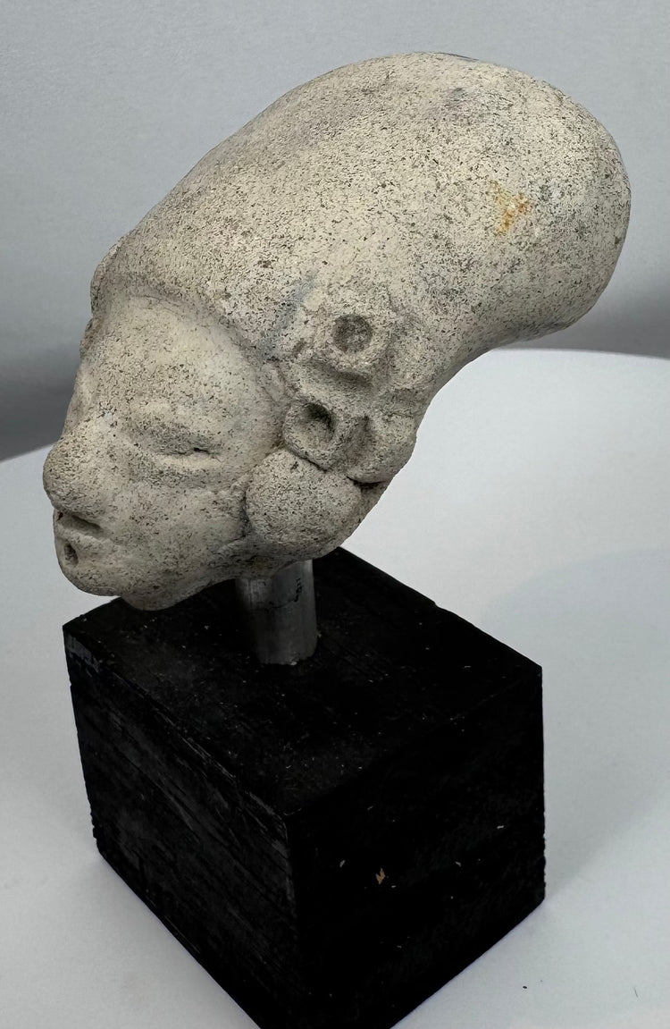 Pre-Columbian funerary terracotta head fragment with closed eyes and weathered archaeological surface.