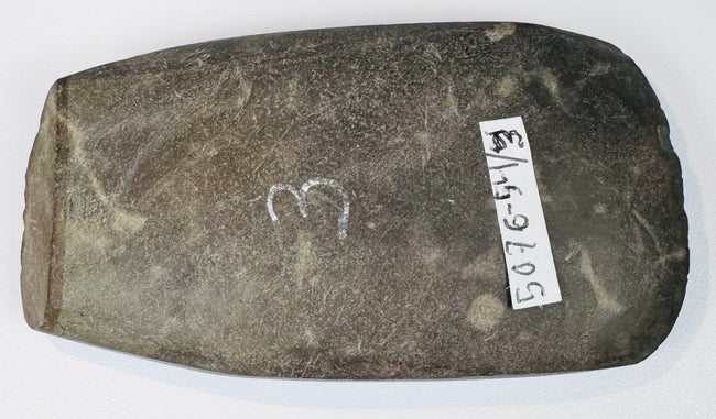 Angled view of an ancient South American ground stone axe with rounded edge from repeated sharpening and historic use.
