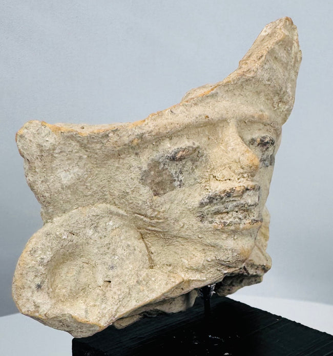 Ancient terracotta ceremonial fragment with fan-shaped crest, human visage, and remnants of dark pigment.