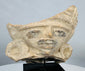 Ancient Mesoamerican terracotta face fragment featuring prominent spiral ear ornaments and traces of original pigment.