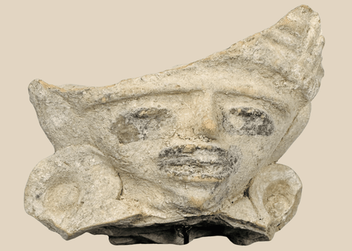 Pre-Columbian terracotta figural fragment depicting a stylized human face with large earspools and fan-shaped headdress, Mesoamerica, circa 600–1200 CE.