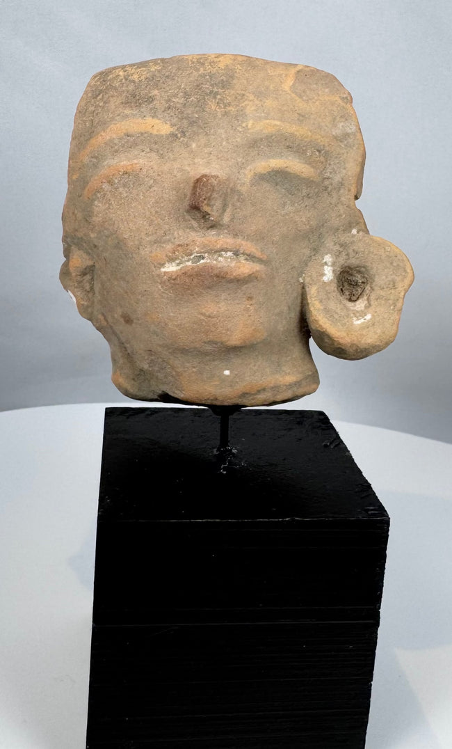 Ancient Mesoamerican ceramic head sculpture fragment with weathered surface and ear ornament.