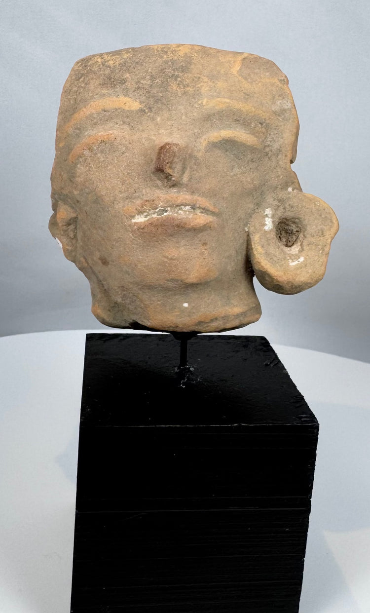 Ancient Mesoamerican ceramic head sculpture fragment with weathered surface and ear ornament.