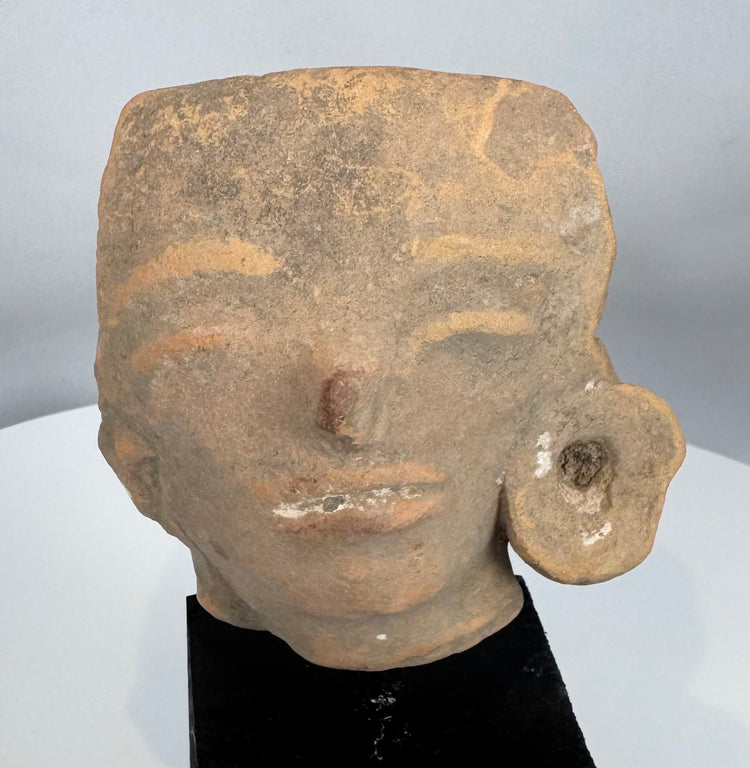 Ancient West Mexican ceramic head fragment depicting stylized facial features and preserved ear ornament.