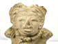 Detail of upper figure's closed slit eyes and elaborate headdress on light brown clay