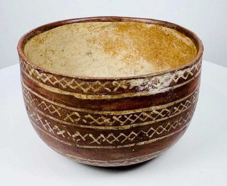 Bichrome pottery bowl featuring cream geometric ornament on a reddish-brown surface.
