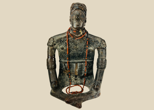 Front view of Pre-Columbian seated shamanic terracotta figure with red beads and headdress on a beige background.