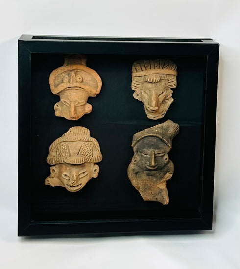Group of four Pre-Columbian terracotta mask or face fragments, mounted together in a black display frame against a white background, showing varied expressions and headdresses.