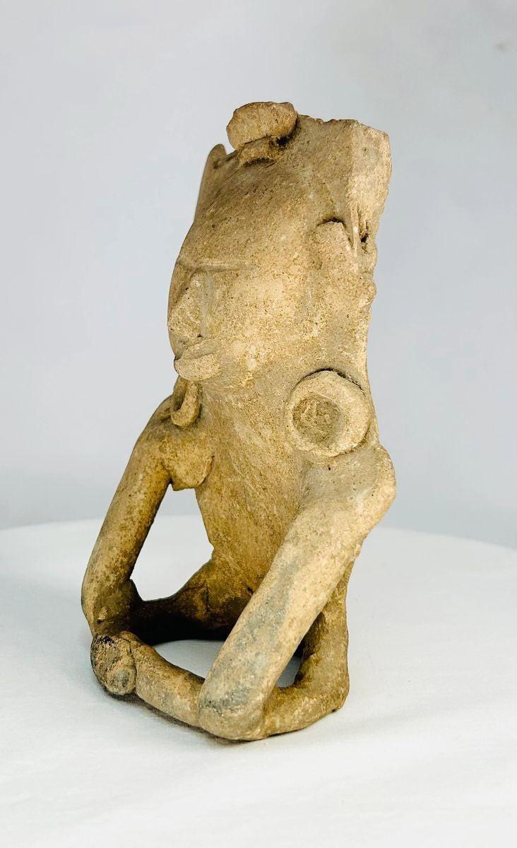 Ancient Mesoamerican terracotta figurine depicting a seated human with helmet-like headpiece, large circular ear ornaments, and hollow cavity in back for ritual use, Classic Period (200–800 AD).