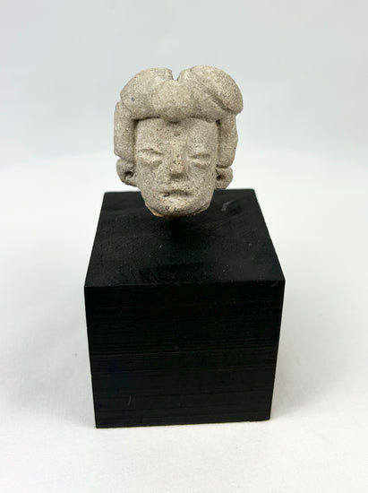 Ancient Pre-Columbian terracotta head fragment from West Mexico, Nayarit/Jalisco shaft-tomb culture, with almond-shaped eyes, straight nose, and stylized coiffure, mounted on a black display base, photographed on a white background.