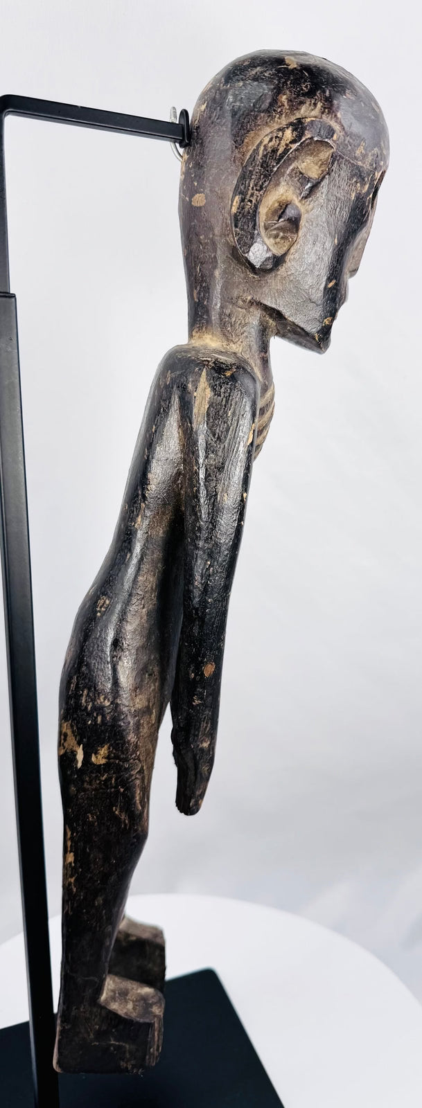 Side view of elongated moai kavakava-inspired wooden sculpture on black display stand