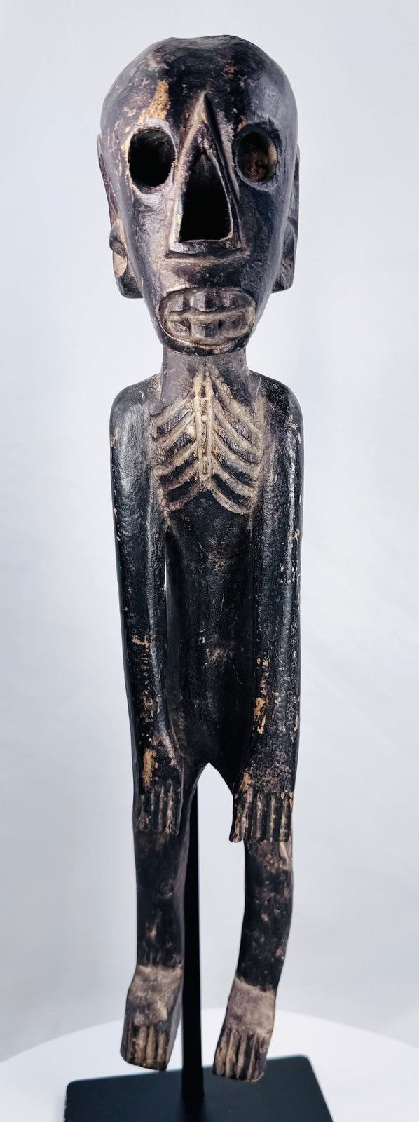 Front view of carved Polynesian-style moai kavakava figure with hollow eyes and rib cage
