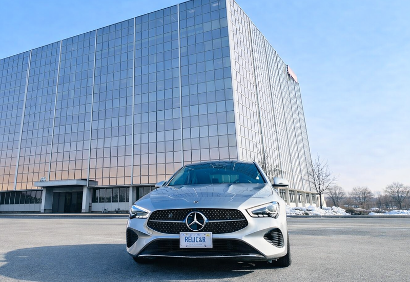 Front view of a white Mercedes-Benz parked outside Relic & Rarity’s modern glass office building at 7030 Woodbine Avenue in Markham, Ontario.