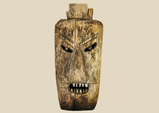 Front view of early 20th-century ritual hardwood mask from Northern Thailand or Laos showing angular features and deep-set eyes.