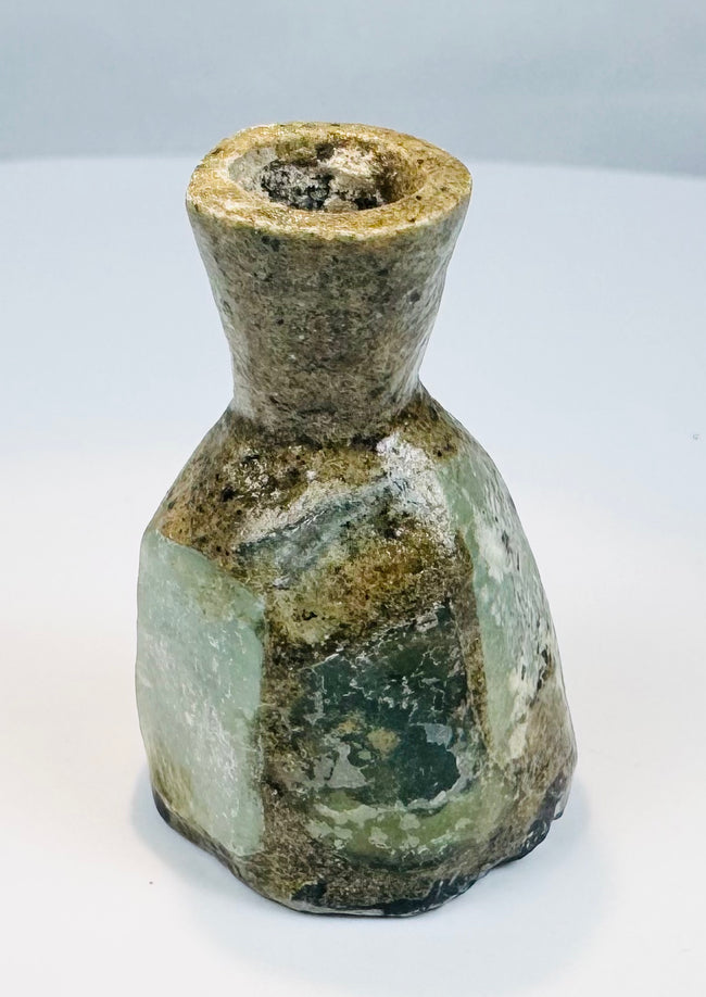 Ancient blown green glass flask with cylindrical neck and weathered archaeological surface
