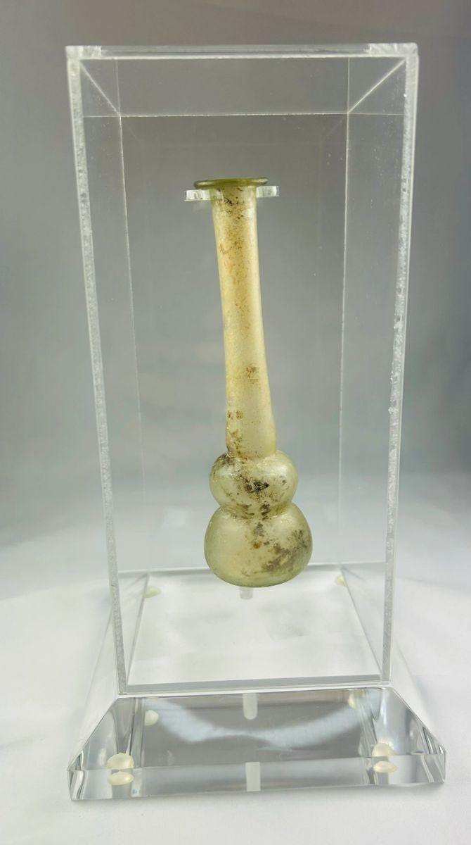 Ancient Roman clear glass double gourd balsamarium from the Eastern Mediterranean, 2nd–3rd Century CE. Features two globular sections joined by a slender neck, naturally iridescent patina, and substantial size for holding perfumes or balms. Reflects Roman glassmaking sophistication, luxury, and daily bathhouse culture.