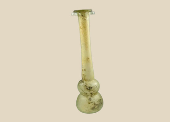 Ancient Roman clear glass double gourd balsamarium from the Eastern Mediterranean, 2nd–3rd Century CE. Features two globular sections joined by a slender neck, naturally iridescent patina, and substantial size for holding perfumes or balms. Reflects Roman glassmaking sophistication, luxury, and daily bathhouse culture.