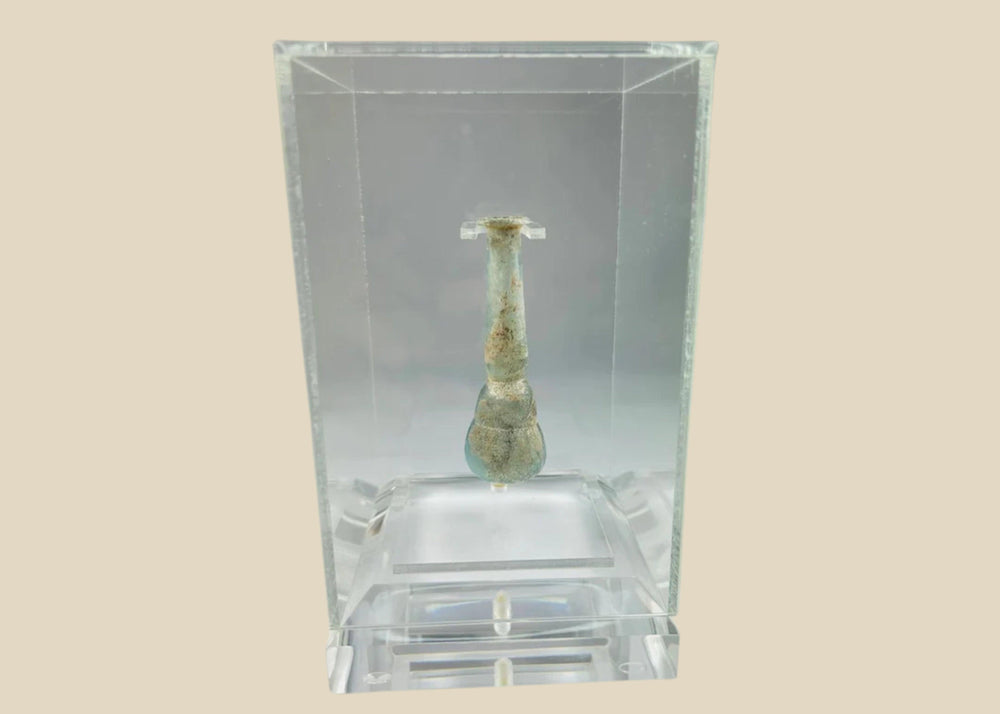 Ancient Roman pale turquoise blown glass balsamarium, 2nd–3rd Century CE. Double-gourd body with tapering neck and outfolded lip, featuring natural iridescent patina. Hand-blown vessel used for perfumes, ointments, and luxury grooming, reflecting Roman craftsmanship, refinement, and elite culture.