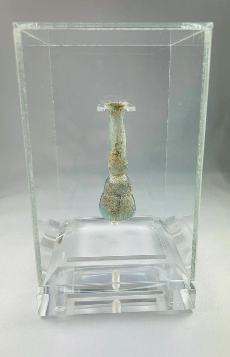Ancient Roman pale turquoise blown glass balsamarium, 2nd–3rd Century CE. Double-gourd body with tapering neck and outfolded lip, featuring natural iridescent patina. Hand-blown vessel used for perfumes, ointments, and luxury grooming, reflecting Roman craftsmanship, refinement, and elite culture.