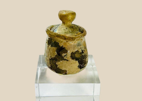 Ancient Roman or Parthian glass cosmetic jar, circa 2nd–3rd century CE, with rounded body, fitted lid topped by a knob finial, and luminous iridescent patina developed over centuries.
