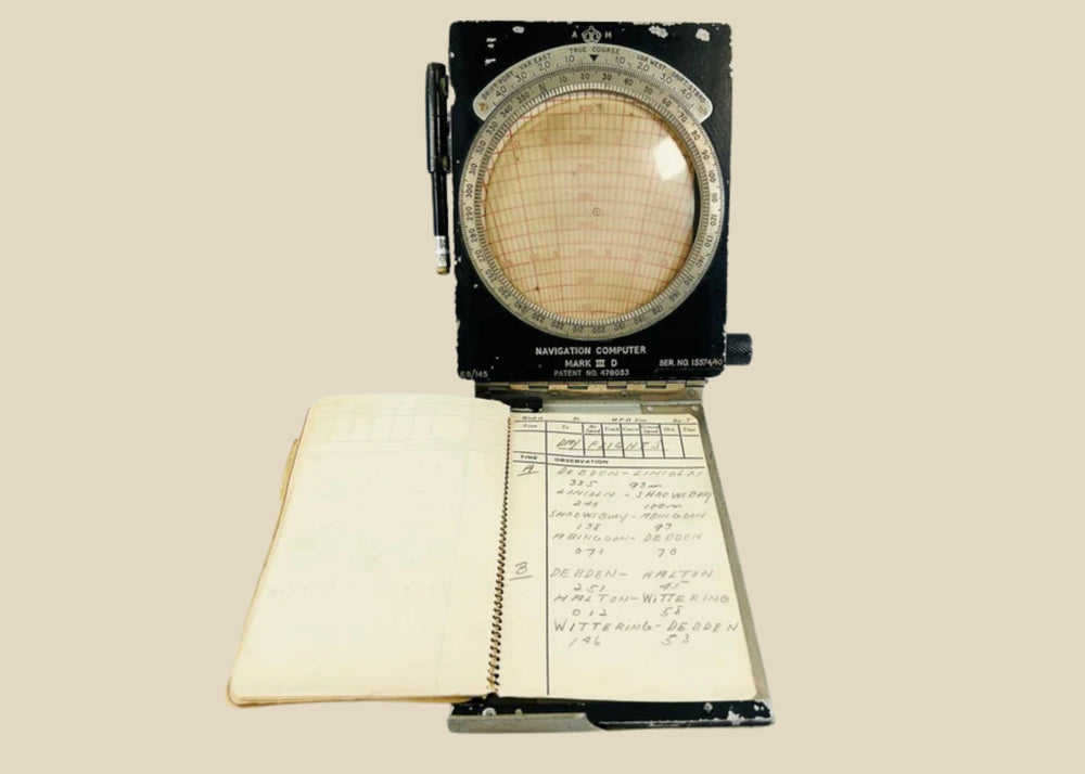 RAF WWII navigational computer with rotating aluminum dial, Bakelite adjustments, original fabric straps, pencil, and open flight notebook showing handwritten navigator’s notes.