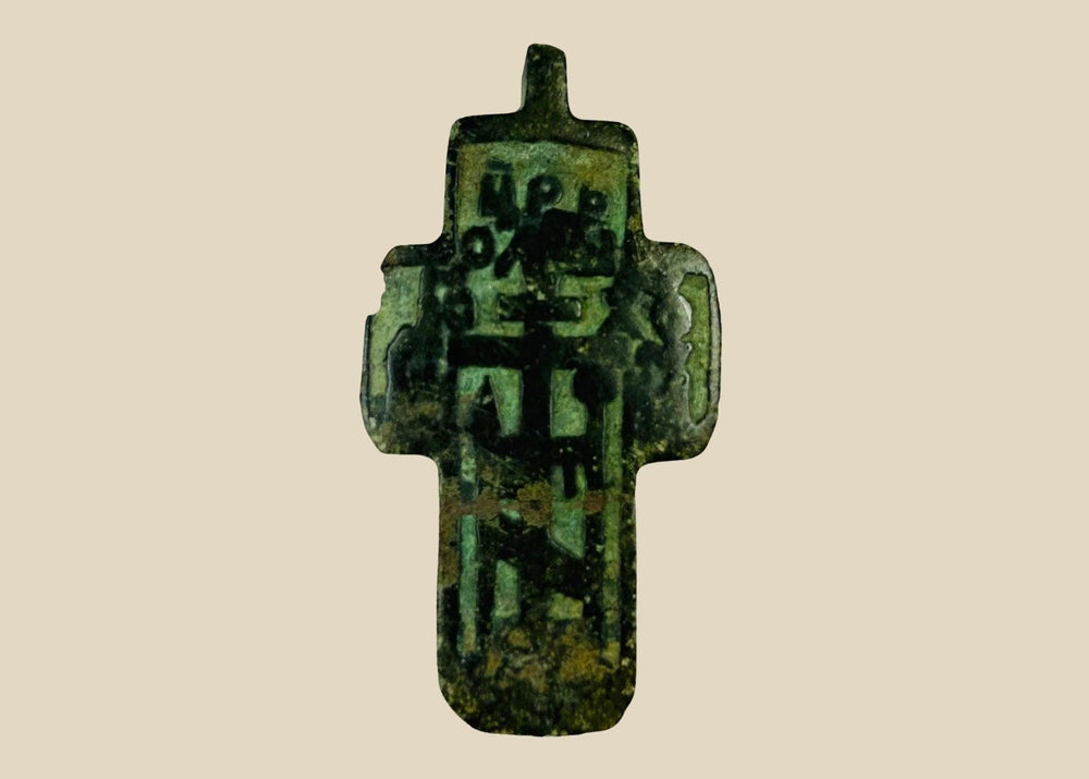 Small Russian Orthodox devotional cross-plaquette from the Old Believer tradition, cast in copper-alloy with champlevé green enamel remnants, blocky Cyrillic inscription panels, and deep olive patina, circa 1780–1820.