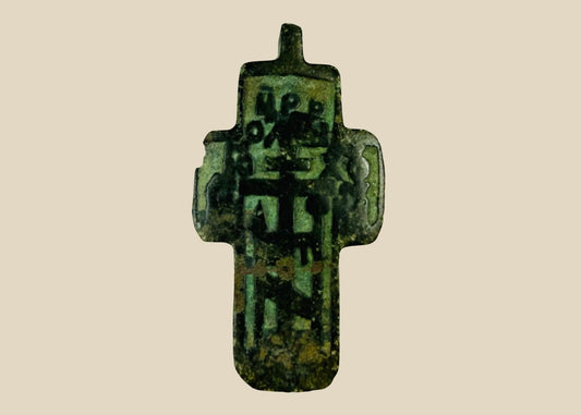 Small Russian Orthodox devotional cross-plaquette from the Old Believer tradition, cast in copper-alloy with champlevé green enamel remnants, blocky Cyrillic inscription panels, and deep olive patina, circa 1780–1820.