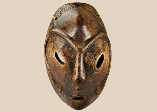 Early 20th-century Sepik River tribal ceremonial mask, hand-carved from wood with elongated oval form, large almond-shaped eyes, incised swirling patterns, and traces of natural pigments, mounted on a display stand; traditional artifact used in ancestral rituals and cultural ceremonies of Papua New Guinea.
