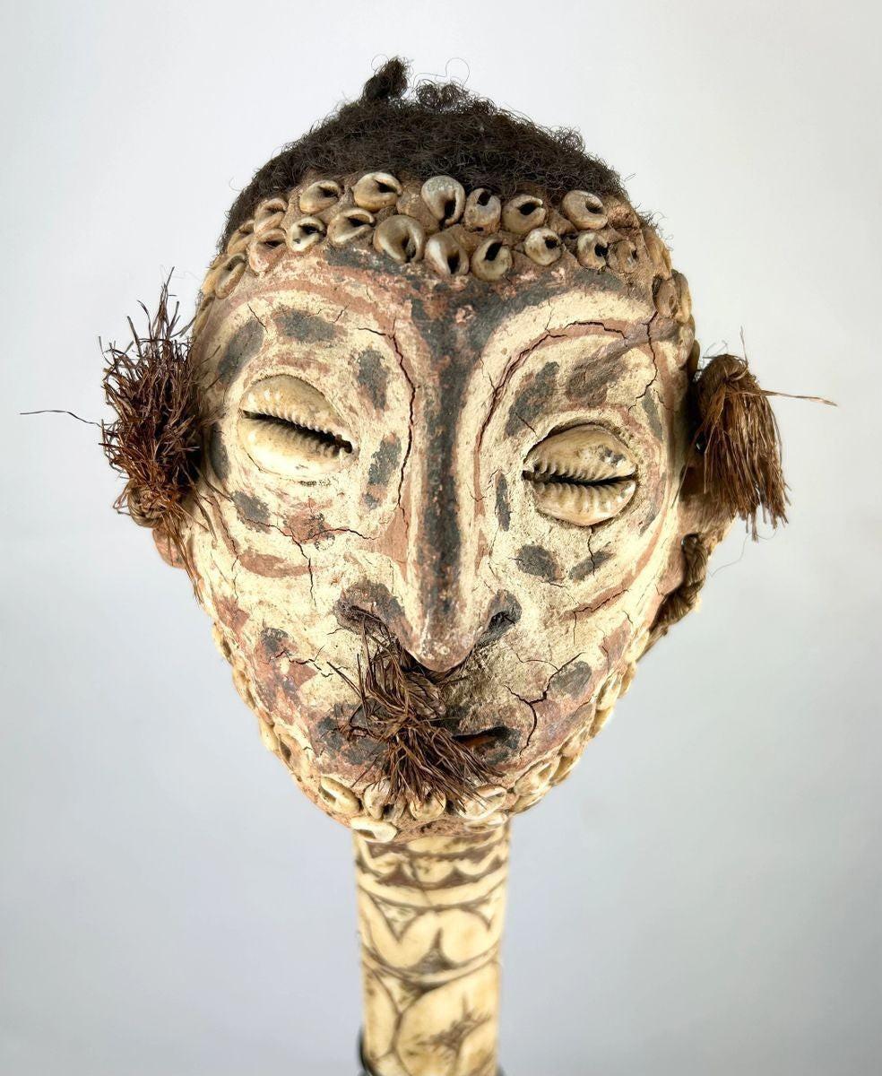 19th-century Sepik River ceremonial bone dagger with carved ancestral head, cowrie shell inlays, human hair adornments, and tribal geometric motifs, used in ritual and initiation rites.