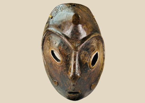 Early 20th-century Sepik River tribal ceremonial mask, hand-carved from wood with elongated oval form, large almond-shaped eyes, incised swirling patterns, and traces of natural pigments, mounted on a display stand; traditional artifact used in ancestral rituals and cultural ceremonies of Papua New Guinea.