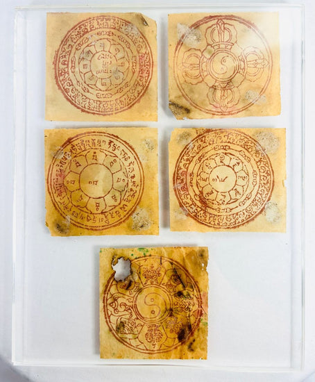 Five circular Tibetan astrological yantras hand-printed in red ink on traditional handmade paper, featuring lotus petals, Eight Auspicious Symbols, and yin-yang motifs, mounted in a modern acrylic display panel, circa 1800s–early 1900s, Tibet/Himalayan Plateau.