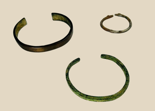 Rare set of three ancient bracelets from the Near East (Mesopotamia to Levant or Anatolia), Bronze to Iron Age (circa 6th millennium BCE – 7th century CE). Includes a broad bronze cuff with green patina, a slender oxidized bronze bracelet, and a textured iron bracelet, reflecting ancient metallurgical skill, decorative traditions, and cultural symbolism of personal adornment.