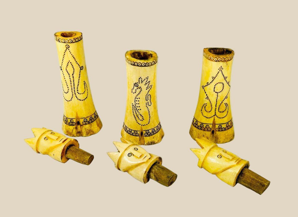 Set of three early 20th-century Indonesian carved buffalo bone lime containers with intricate scrimshaw motifs and lids topped with crowned royal figures, used in traditional betel nut chewing rituals.