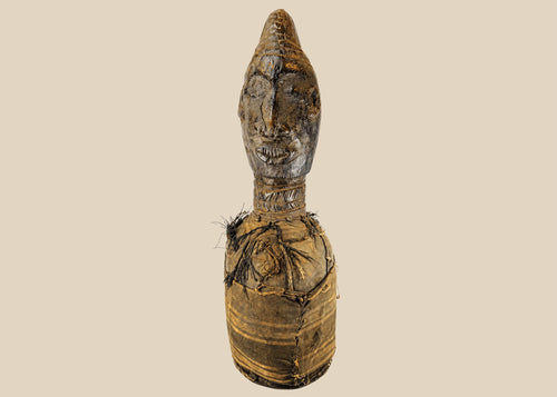Hand-carved Central or West African wooden figure with elongated facial features, natural fiber torso wrapping, and traces of organic pigments, standing on a white background.