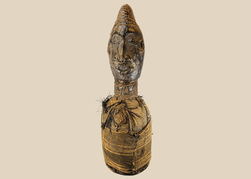 Hand-carved Central or West African wooden figure with elongated facial features, natural fiber torso wrapping, and traces of organic pigments, standing on a white background.
