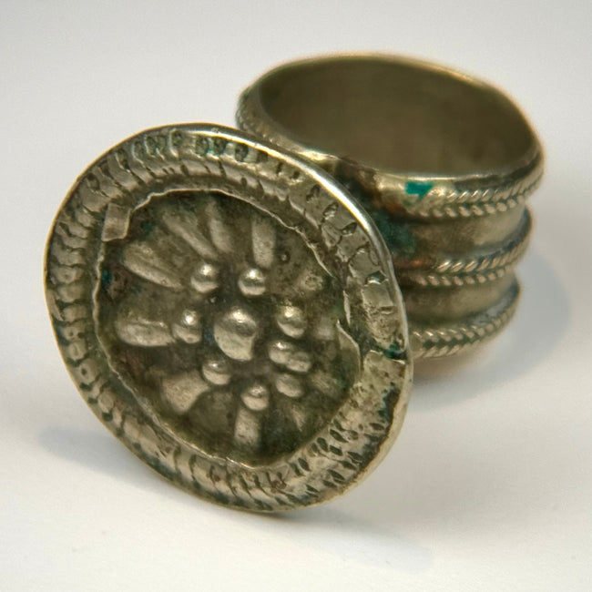 Antique silver-colored ring featuring a raised floral rosette design within a round decorative bezel