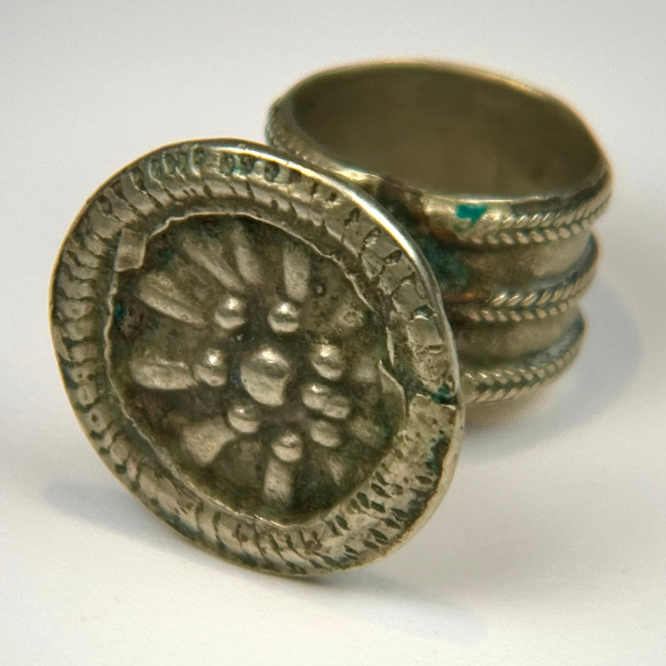 Antique silver-colored ring featuring a raised floral rosette design within a round decorative bezel