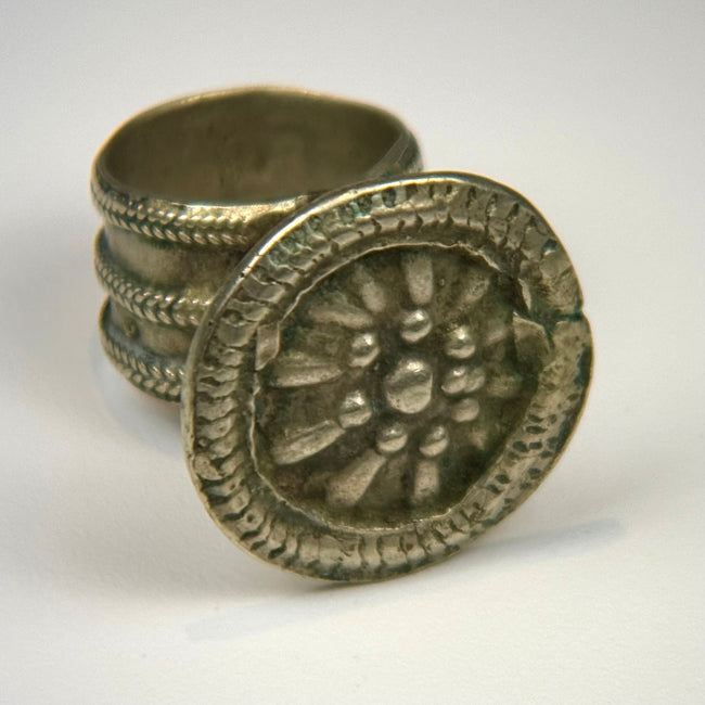 Antique silver-toned ring with circular floral bezel, detailed relief work, and natural surface patina