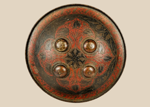Small circular Indo-Persian Dhal shield, 11 inches diameter, lacquered black and red with damascened foliate motifs, four raised bosses, interior grips with knuckle-guard cushion, well-preserved antique.