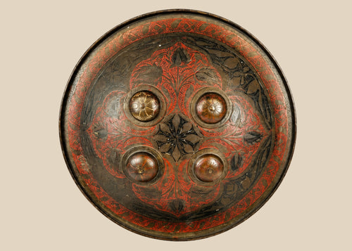 Small circular Indo-Persian Dhal shield, 11 inches diameter, lacquered black and red with damascened foliate motifs, four raised bosses, interior grips with knuckle-guard cushion, well-preserved antique.