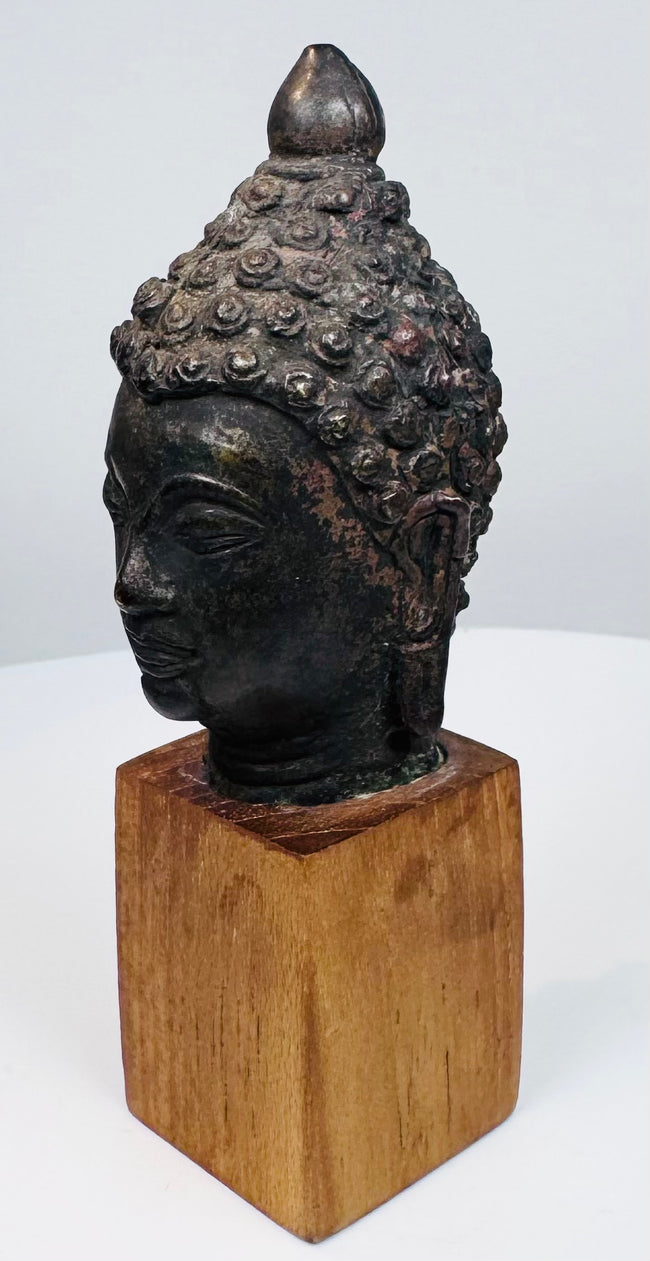 Antique bronze Buddha head with serene expression, closed eyes, and detailed hair curls
