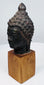 Antique bronze Buddha head with serene expression, closed eyes, and detailed hair curls