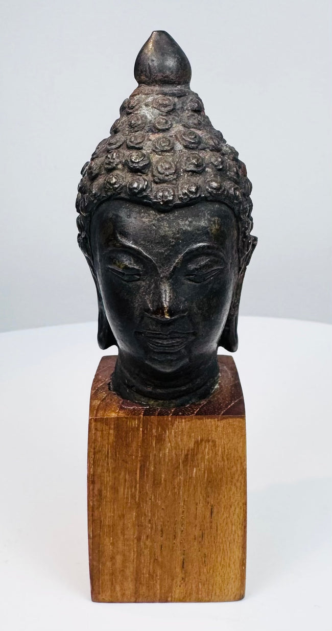 Cast bronze Buddha head with finely detailed hair, tranquil expression, and wooden display base