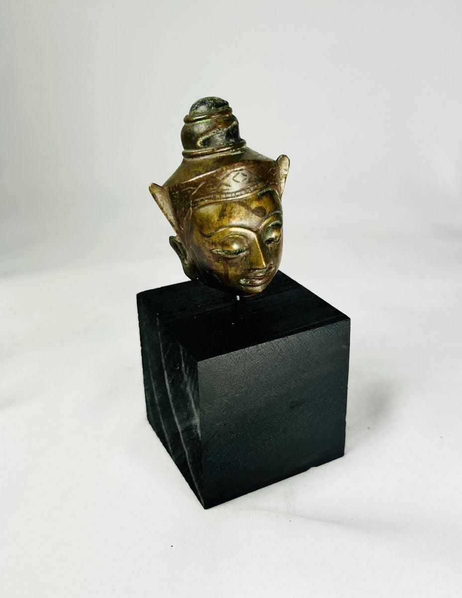 Bronze Buddha head on black display base, featuring serene facial expression, pointed ushnisha, and natural greenish patina, likely from Thailand or Cambodia, 18th–19th century CE.