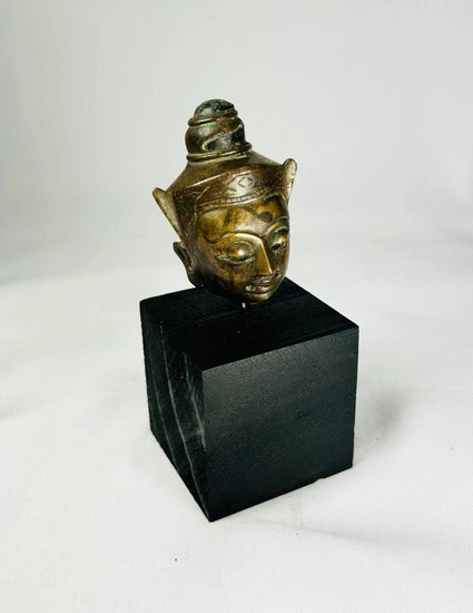 Bronze Buddha head on black display base, featuring serene facial expression, pointed ushnisha, and natural greenish patina, likely from Thailand or Cambodia, 18th–19th century CE.