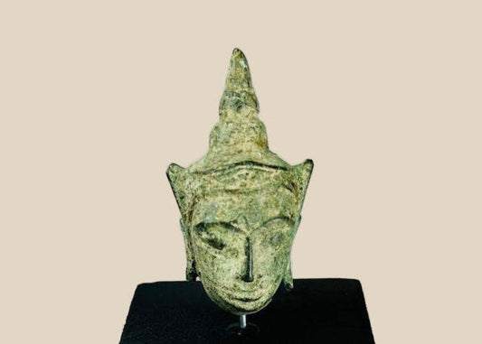 Small antique Southeast Asian bronze Buddha head, likely from Thailand or Cambodia, 16th–17th Century CE. Features serene expression, elongated earlobes, pointed ushnisha, and natural green patina. Originally part of a larger statue, serving as a devotional object reflecting Buddhist spiritual symbolism, artistry, and enlightenment.