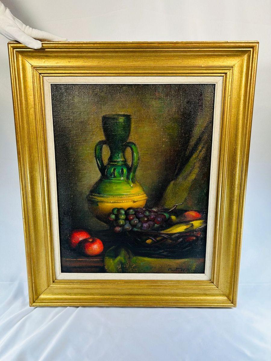 Mid-20th century still life oil painting depicting a green vase, grapes, and apples on a tabletop. Signed by the artist, framed in a gilded wooden frame, with rich colors and detailed brushwork.