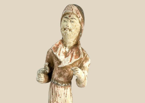 Tang Dynasty low-fired terracotta figure of a female court attendant, standing with hands clasped, wearing flowing robes with traces of red and white pigments, serene expression, Tang hairstyle, 13 inches tall, surface mineral deposits and patina, circa 618–907 CE.