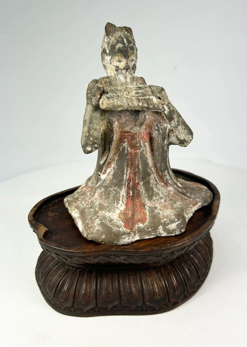 Tang Dynasty terracotta figure of a seated female court musician playing a pan flute, traces of red and white pigments, displayed on a carved wooden stand, 7th–9th century China.
